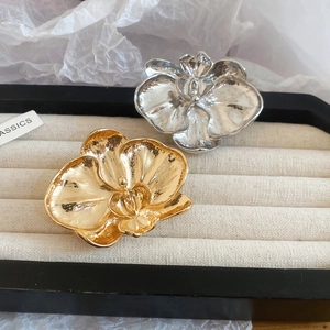Detail view of gold and silver flower brooches with hammered texture on beige jewelry tray