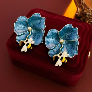 Macro shot of blue enamel flower earrings with gold bee detail on red velvet box