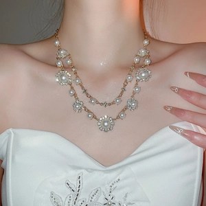 Close-up of double-layer gold necklace with white pearls and sparkling floral pendants