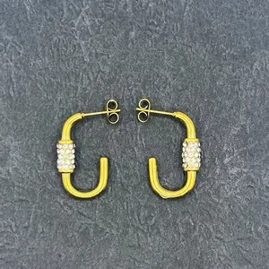 Close-up of U-shaped 18k gold earrings with inlaid pearls and sparkling crystals