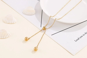 Macro detail of golden Y-necklace featuring matte ball pendants on a white plate
