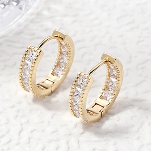 Close-up of golden huggie earrings featuring a row of square-cut clear zircons