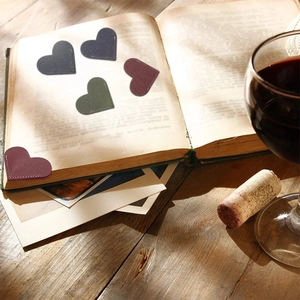 Heart-shaped PU leather bookmarks in dark red, green, and black on vintage book pages