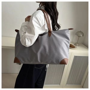 Detailed view of grey nylon tote bag with brown leather handles worn on the shoulder