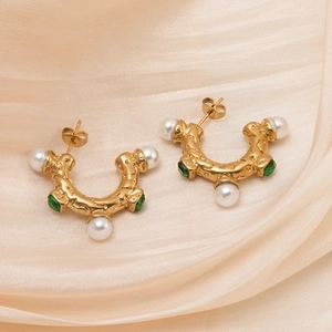 Detail of C-shape stainless steel earrings with white pearls and green gemstones on silk