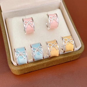 Detail of colorful enamel bow C-shaped stud earrings in pink, blue, and yellow colors