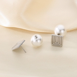 Vista macro de pendientes cuadrados plateados con perlas blancas sobre seda beige