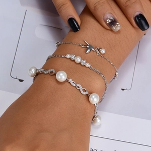 Detailed view of triple-layered silver bracelets with pearl, bird charm and zircon ball