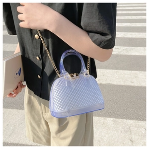 Close-up of light blue PVC shell bag with diamond texture and gold chain on the street