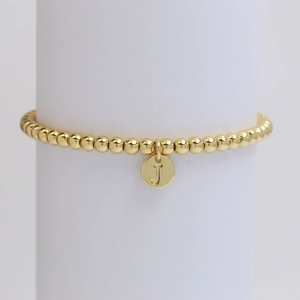 Detail of a gold beaded bracelet featuring a round pendant with engraved letter J