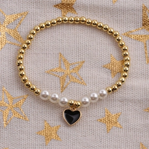 Detail of gold beads and white pearls bracelet featuring a black heart charm on fabric