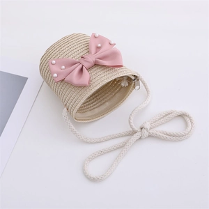 Detailed view of kids straw crossbody bag with pink bow and pearl accents on white background