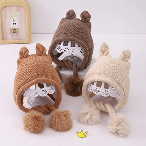 Close-up of winter baby knit hats in three colors with cute ears and fluffy pom-poms
