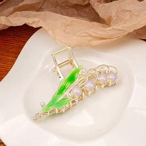 Detail of lily of the valley hair claw with green leaves and pearls on a white plate