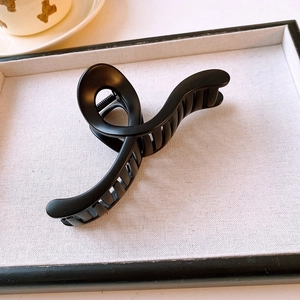 Close-up of a matte black twisted shark hair clip on a textured linen display tray
