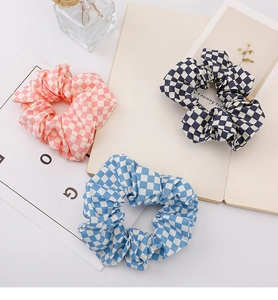 Close-up of three checkered fabric scrunchies in pink, blue, and black grid patterns