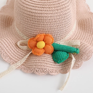 Detail of hand-woven straw hat featuring white lace ties and a colorful knit flower accessory