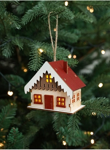 Close-up of a lit wooden Christmas cabin ornament hanging on a festive pine tree branch