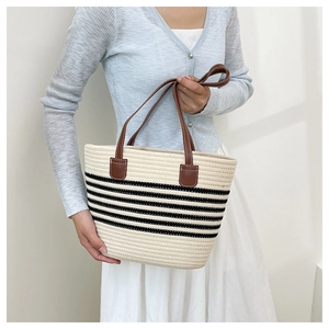 Borsa tote in paglia intrecciata con strisce nere e manici in pelle marrone su modella