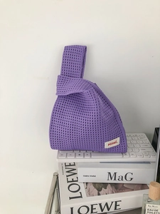 Chic purple knitted knot bag with hollow texture displayed on top of a laptop and books