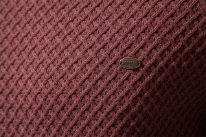 Macro detail of dark red knit sweater featuring a geometric diamond texture and metal tag