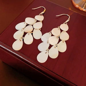 Detailed close-up of shell teardrop tassel earrings on a vintage wooden jewelry box