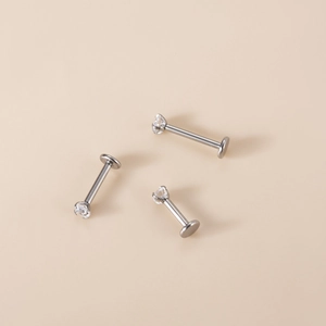 Detailed view of three G23 titanium labret studs with zircon crystals on beige background