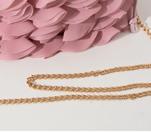 Close-up of pink layered pleated fabric and golden metal chain strap on an evening bag