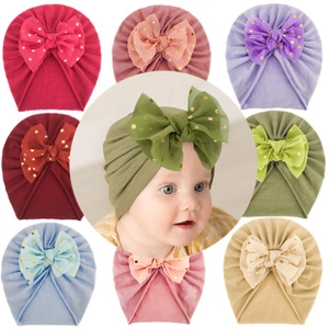 Close-up of soft knitted baby hats with large mesh bows and gold glitter polka dots