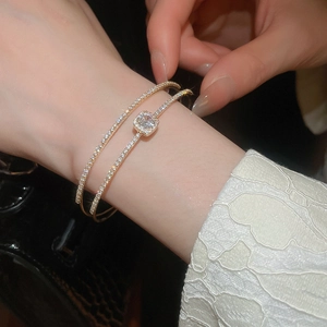 Detail of gold-layered bow bracelets with square zircon accents worn on a wrist