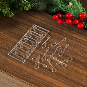 Transparent plastic Christmas hooks on dark wood background with pine and red berries
