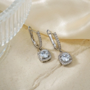 Detail of silver square halo earrings with cubic zirconia on a stone and silk background