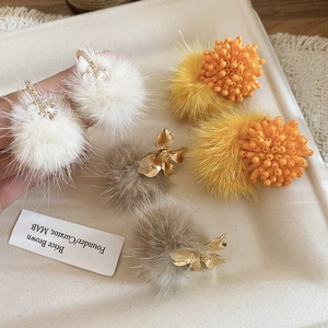 Detailed view of three plush fur pompom earrings with rhinestones and floral elements