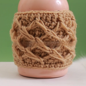 Close-up of handmade crochet mug sleeve with thick khaki knit diamond pattern