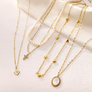 Layered gold necklaces with pearl cross pendant and heart charms on silk background