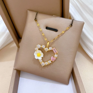 Goldene Herzkette mit rosa Steinen und Emaille-Gänseblümchen auf einem Schmuckkissen