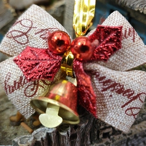 Detail of Christmas ribbon bow with gold bell and red leaves on beige fabric