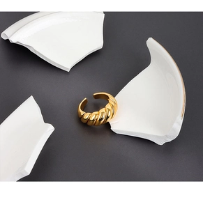 Macro shot of gold croissant dome ring with twisted texture on grey stone and ceramic