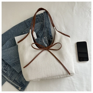 Close-up of beige canvas tote with herringbone texture and large brown leather bow detail