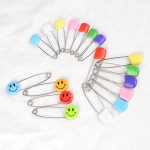 Spille di sicurezza colorate con faccina sorridente e teste in plastica su tessuto bianco