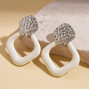 Detail of silver textured earrings with off-white resin hoops on stone background