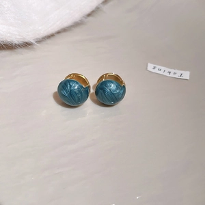 Detail of gold-plated hoop earrings with wavy dark blue enamel finish on textured surface