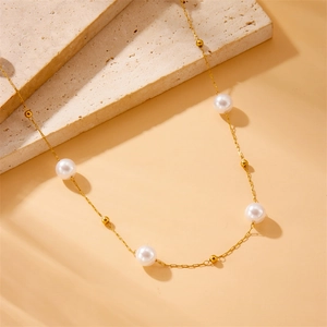 Elegant gold chain necklace with white pearls and gold beads on a beige stone travertine surface