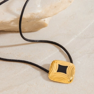 Square gold pendant with black center and wave texture on a black braided cord necklace