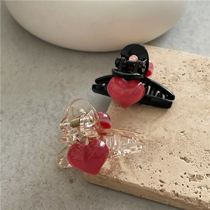 Close-up of black and clear hair claws with red heart accents on stone surface