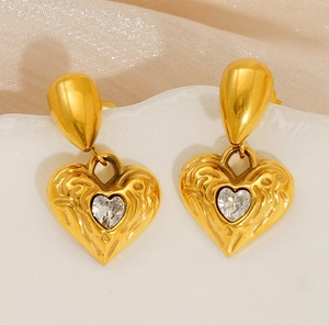 Detailed macro of golden hammered heart earrings with crystal zircon on silk fabric