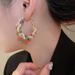 Detail of colorful crystal and pearl beaded hoop earring worn by a model to show size