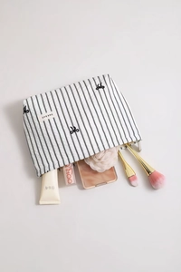 Vue macro de la trousse cosmétique rayée avec nœud brodé noir et détail de fermeture éclair