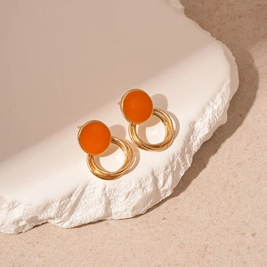 Vintage gold geometric hoop earrings with orange enamel studs on a stone background