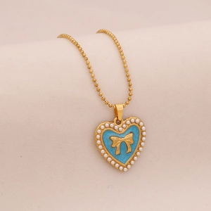 Macro view of blue heart pendant with golden bow and pearl edges on a bead chain